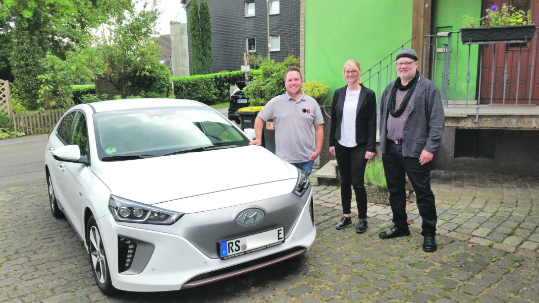 Kevin Bornewasser (emobitec), Maren Koppelberg (EWR) und der erste Besitzer einer EWR-Wallbox zum Laden von E-Autos in der heimischen Garage Stefan Zwanzig-Müller vor einem reinen E-Automobil. Foto: Sascha von Gerishem